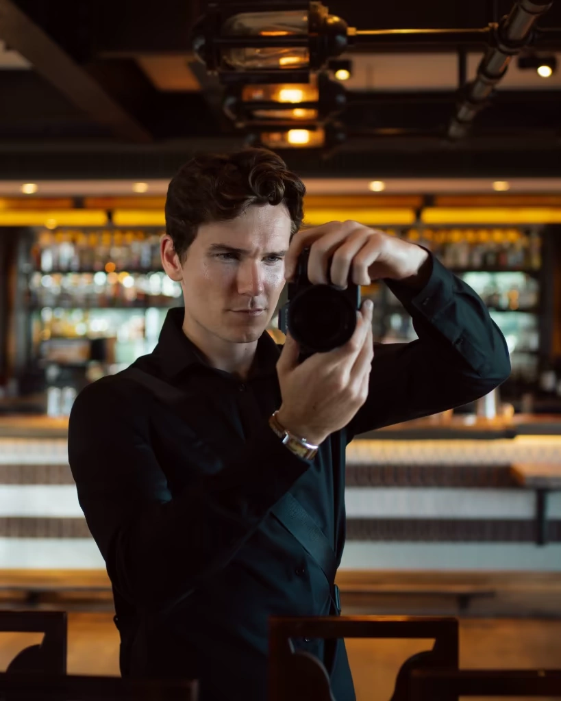 Luke Stimson holding a camera while photographing inside a bar.